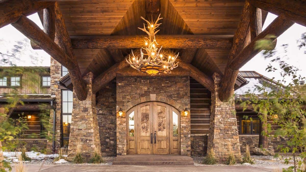 stone around arched doorway on front of log cabin with antler chandelier above door