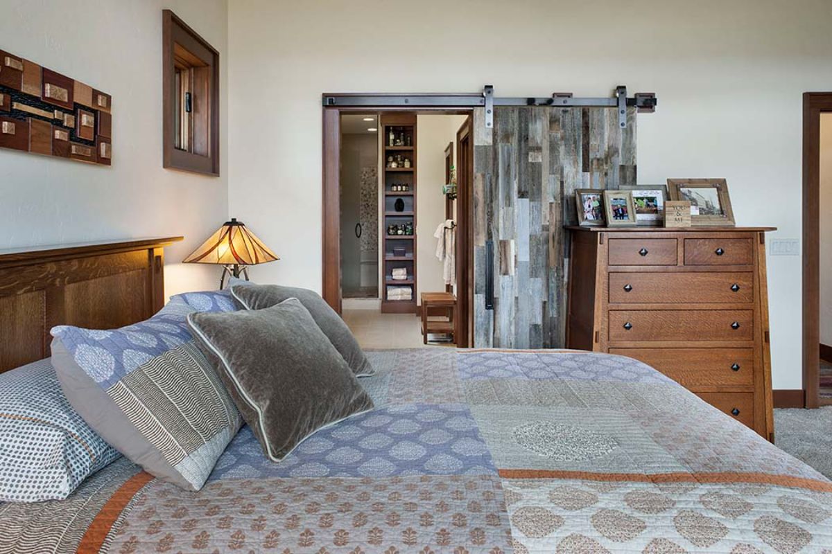 white and light gray bedding on bed looking across room to distressed wood barn door opening