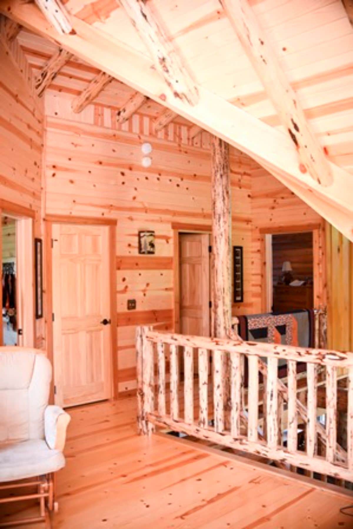 log cabin loft landing with light wood railing and bedroom doors in background