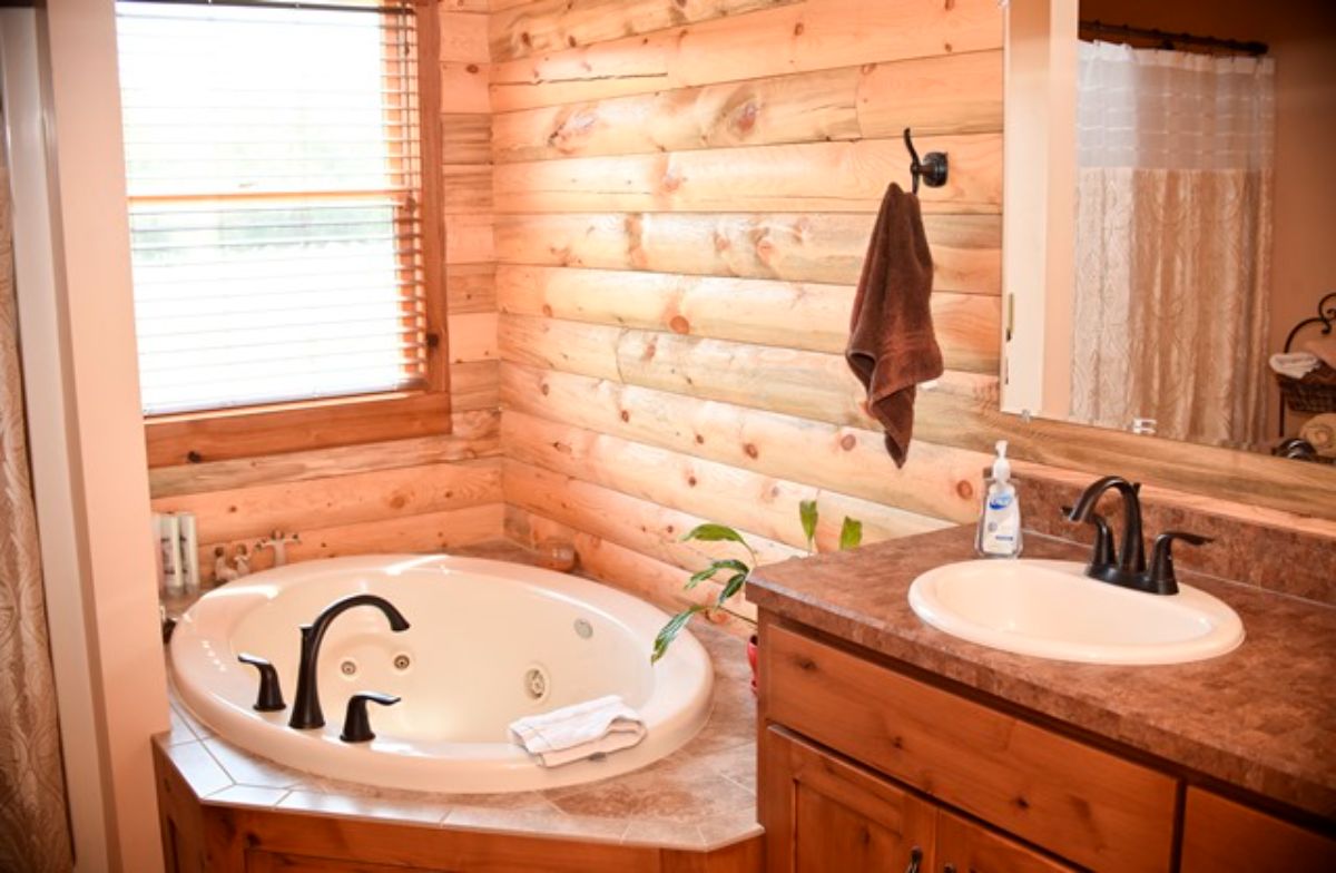 white round soaking tub in corner of log cabin bedroom with dark wood cabinets below white sink