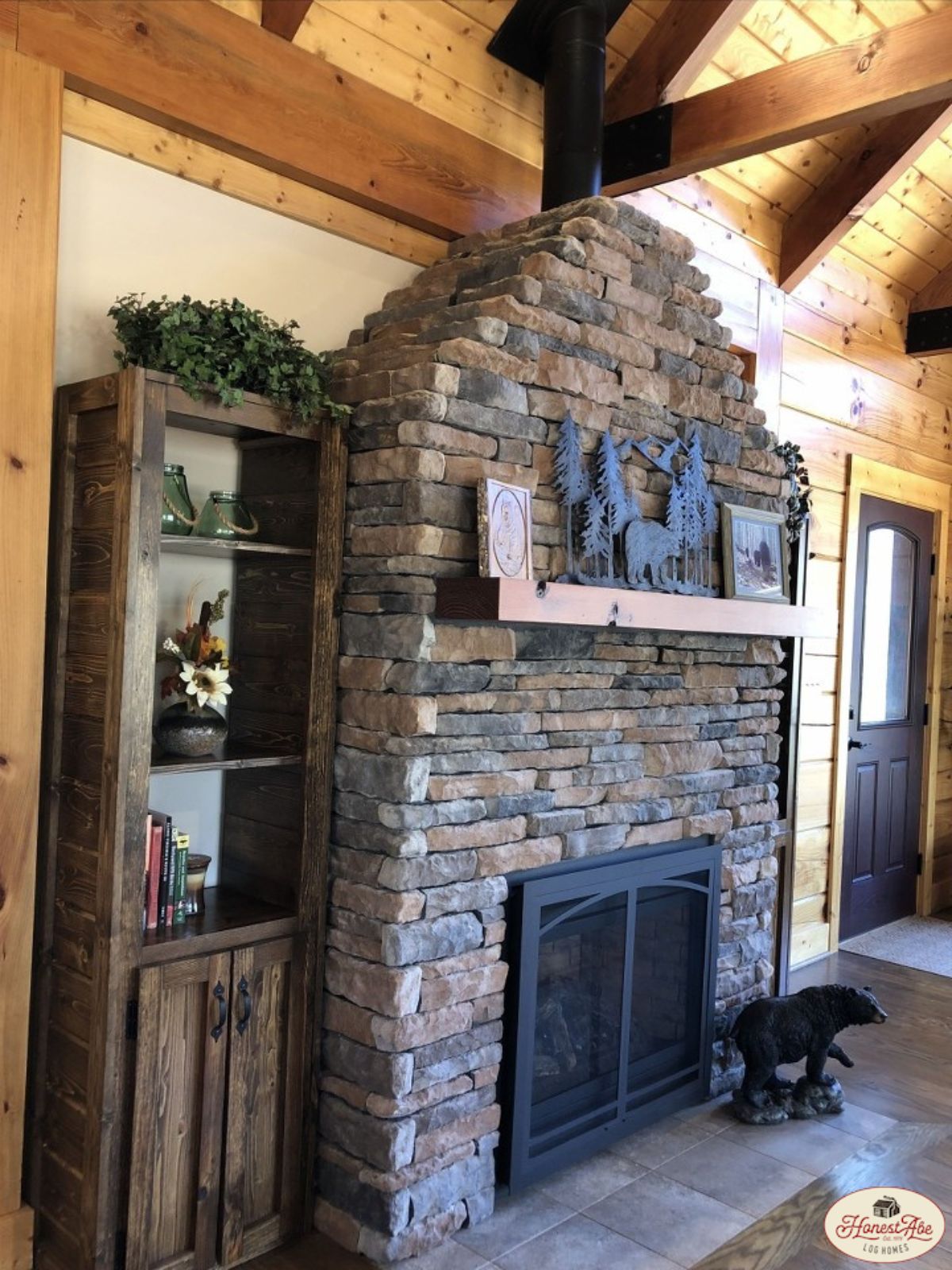 stone fireplace with log mantle and black iron frame in front of opening