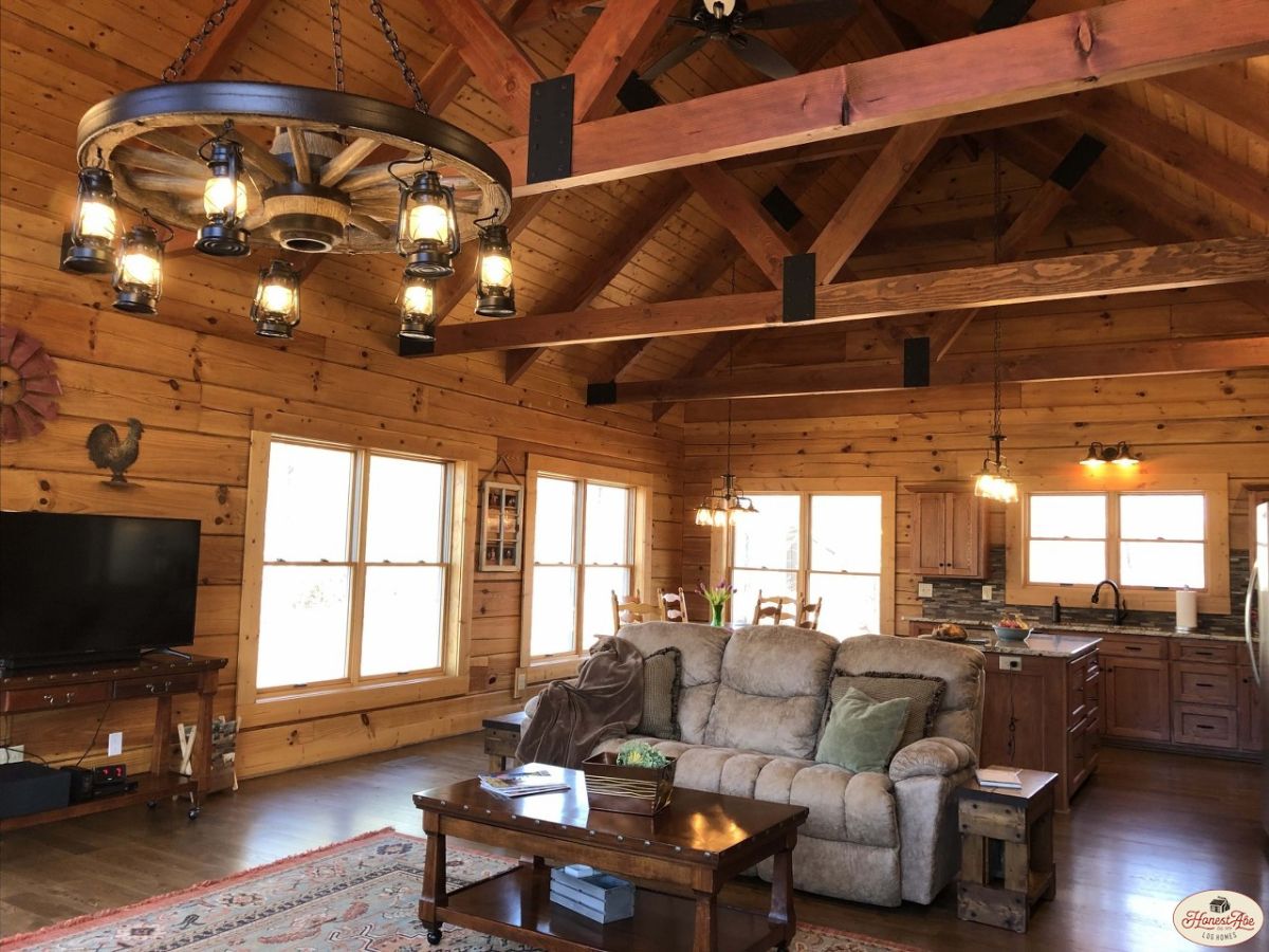 brown recliner sofa behind wood coffee table under round chandelier in cabin