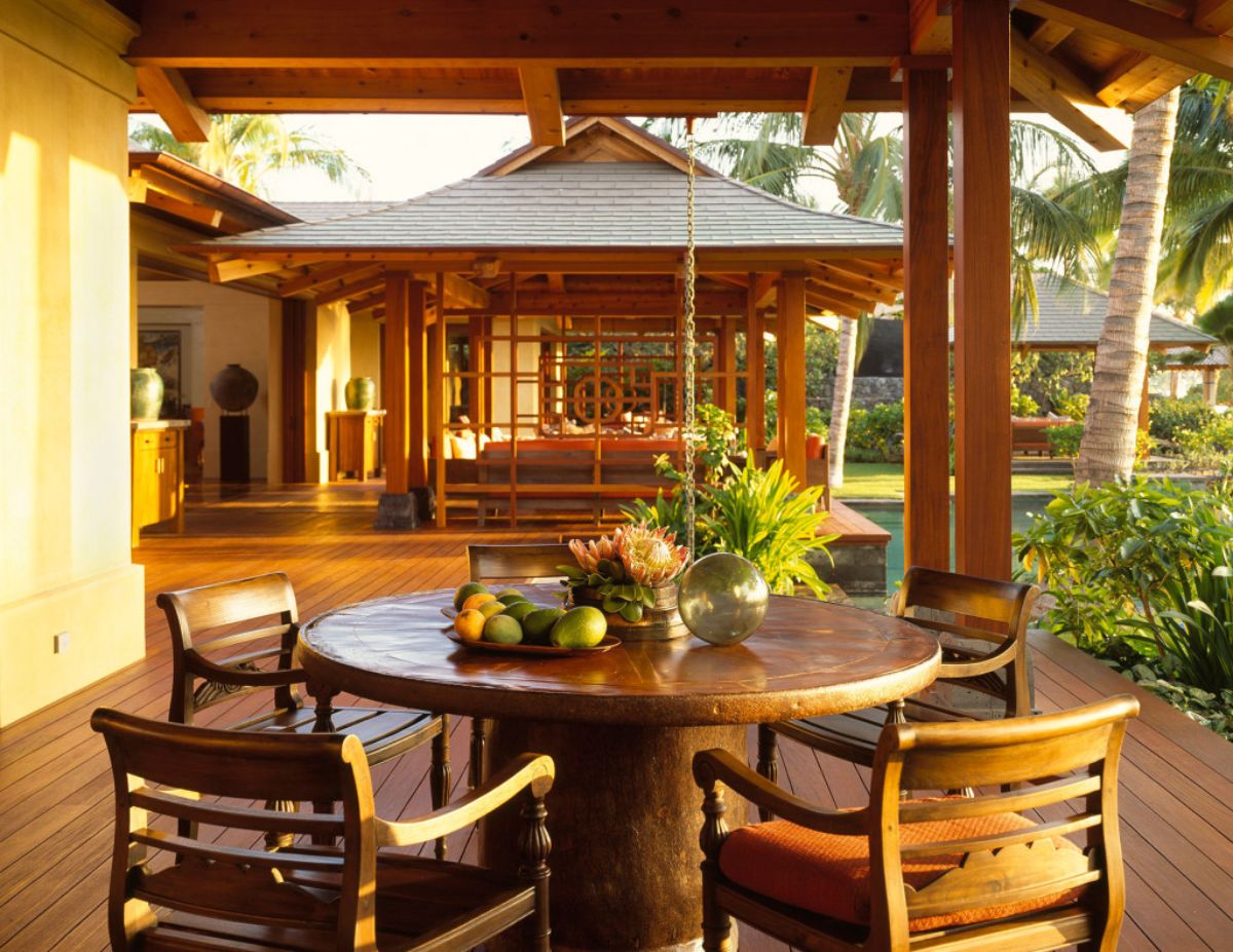 wood round table with wood chairs around it under roof by log cabin