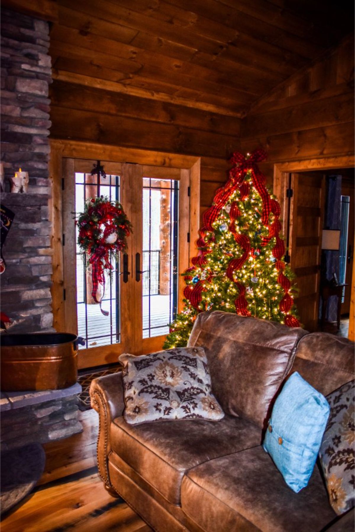 holiday tree behind sofa next to glass french doors of log cabin