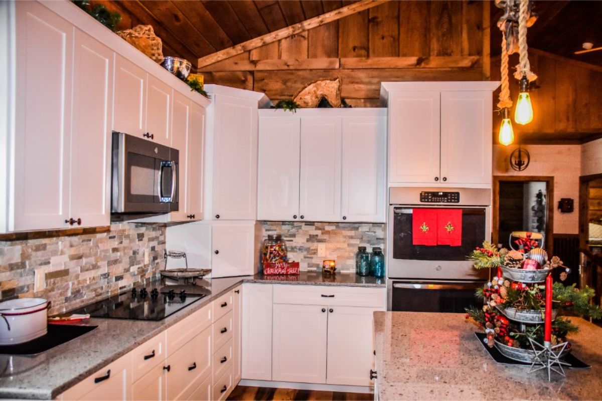 white cabinets in kitchen with white and gray tile back splash and red towel on stove
