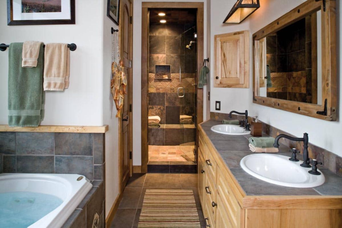 soaking tub with gray tile surround in bathroom with two vanities and tile shower in background