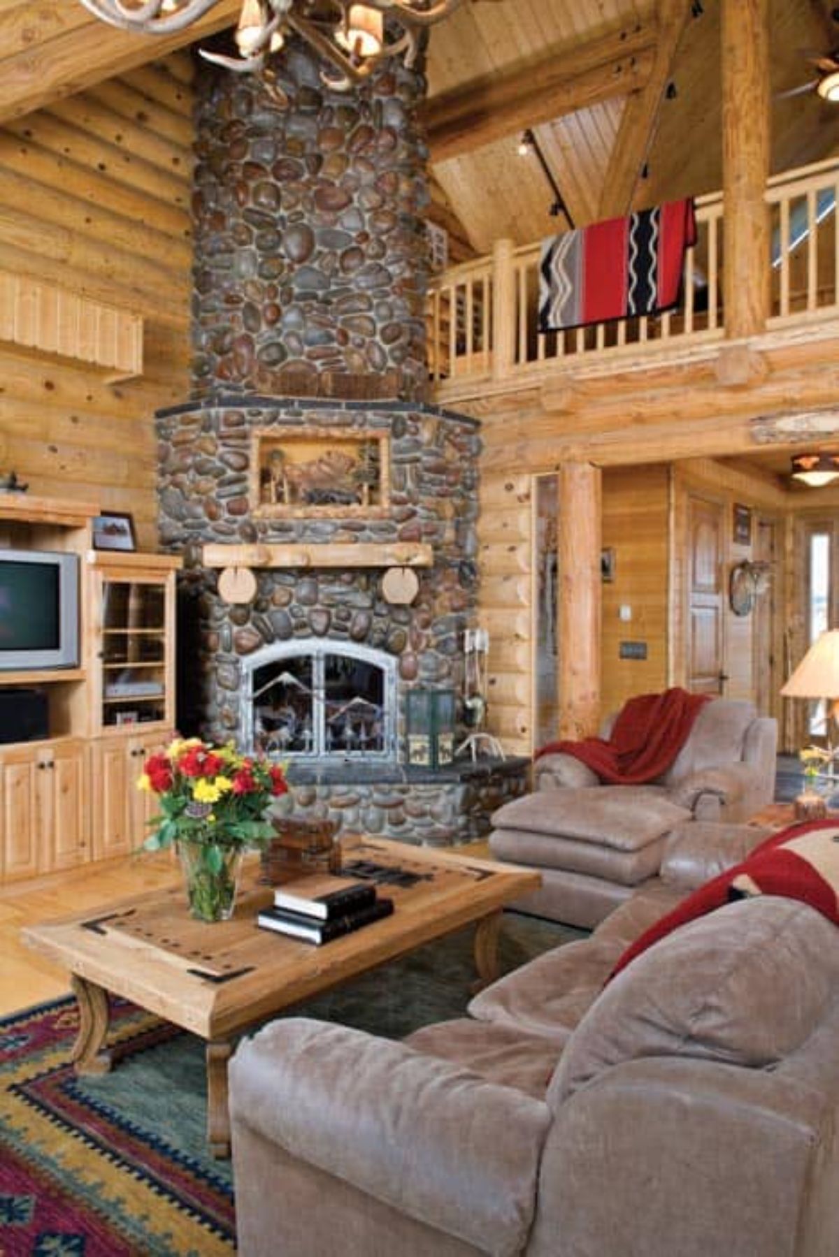 stone fireplace in corner of log cabin with light brown sofas in foreground