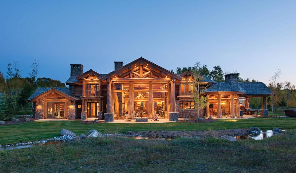sprawling log home with two chimneys and porches lit after dark