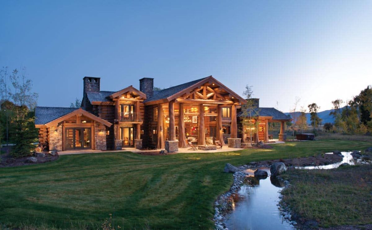 light wood log cabin lit up after dark behind pond