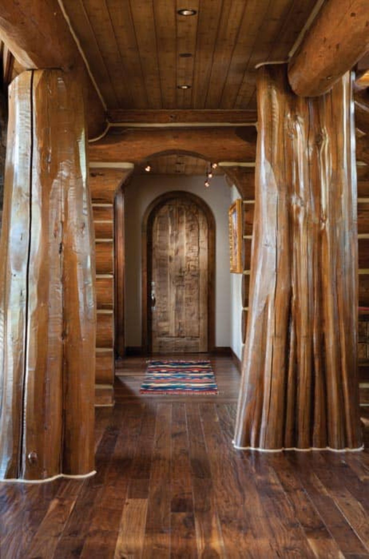 arched wood door at end of hall with log trunks in hall as beams