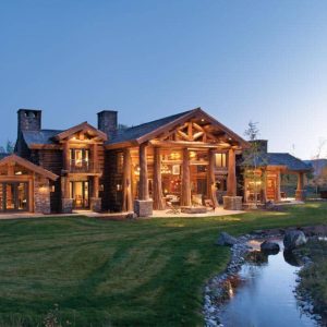 sprawling log home with two chimneys and porches lit after dark
