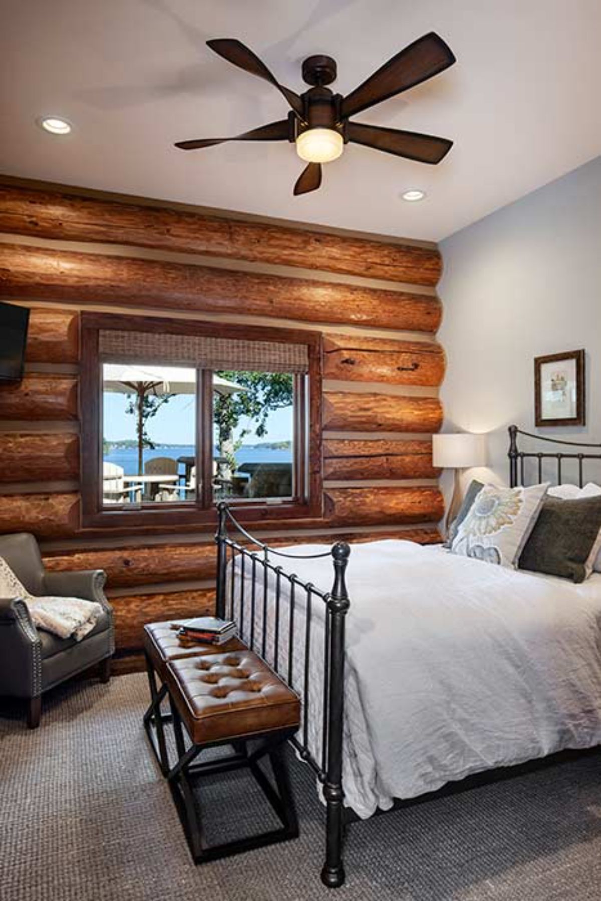 white linens on black iron bedframe in log cabin bedroom with bench at end of bed
