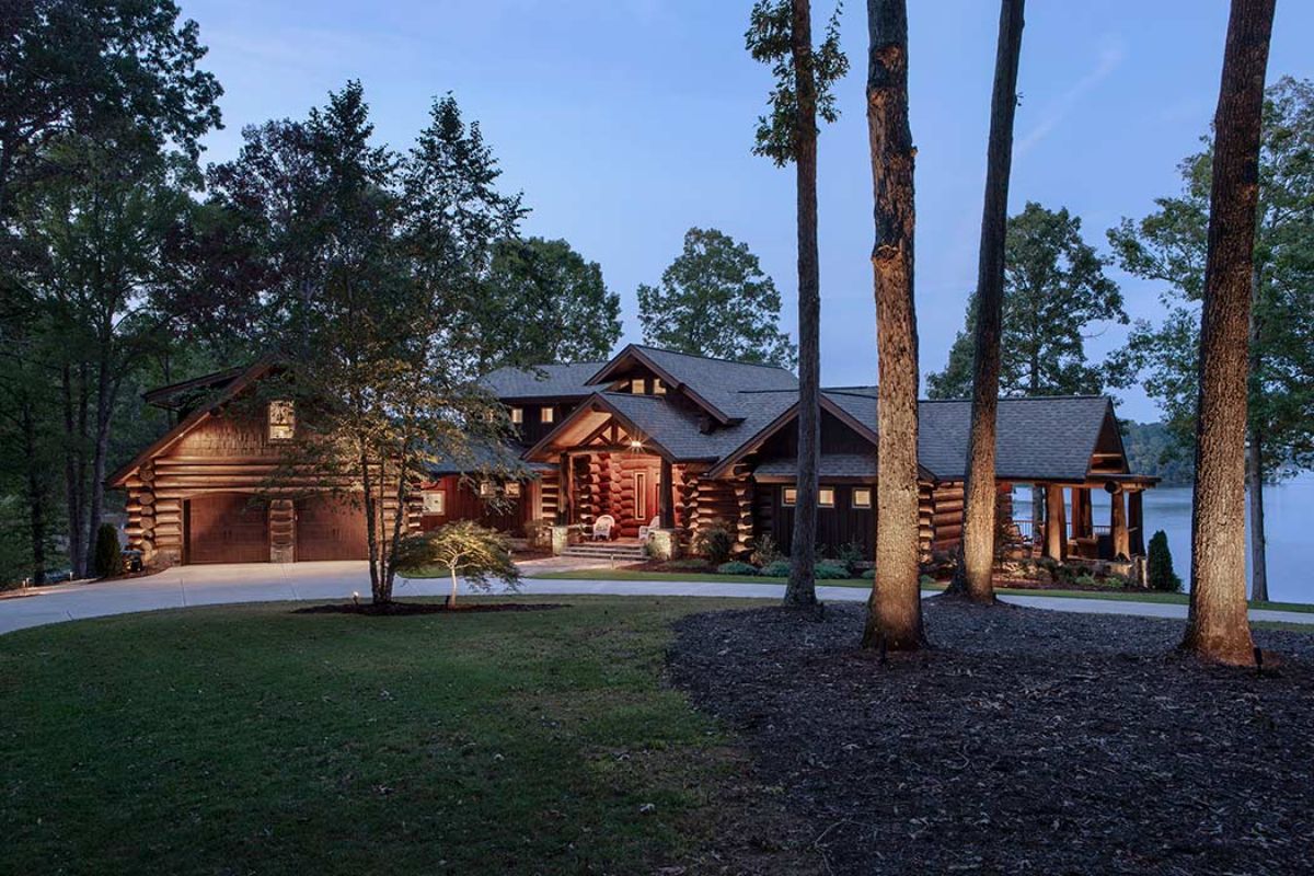 log cabin with 2 car garage and dark stain set back behind trees with concrete driveway