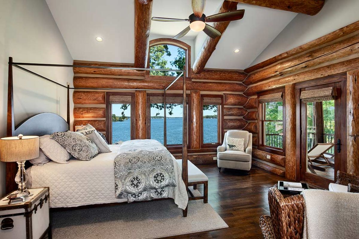 wall of windows overlooking lake behind large wrought iron bed frame with white and gray linens