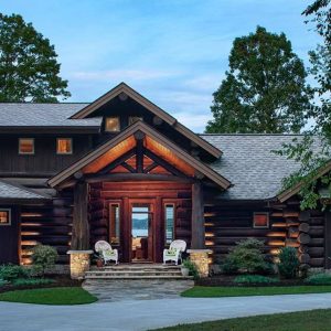 dark stain log cabin with shrubs by walkway and stone steps to covered small porch