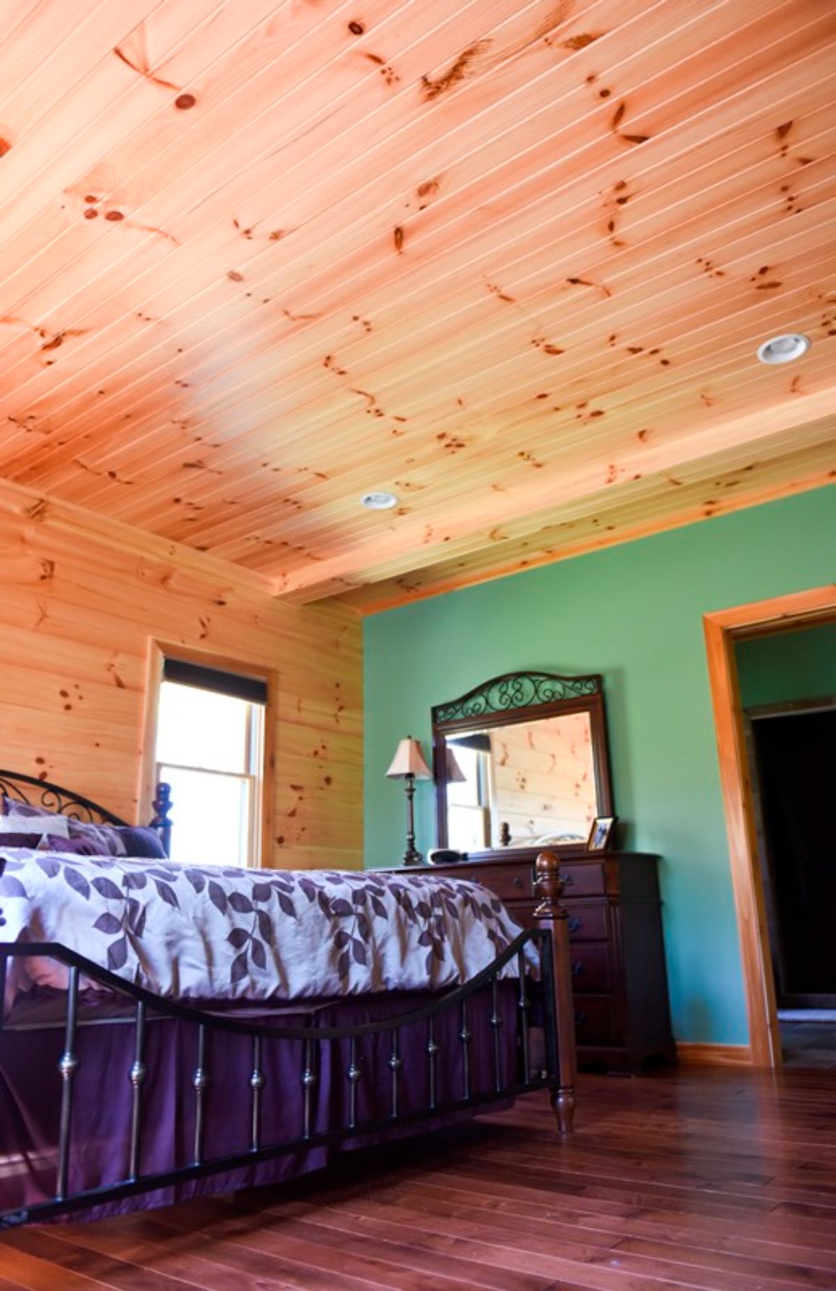 green wall in bedroom of log cabin with wood ceilings