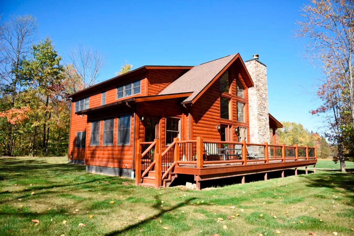 open porch on side of log cabin with chimney on far right