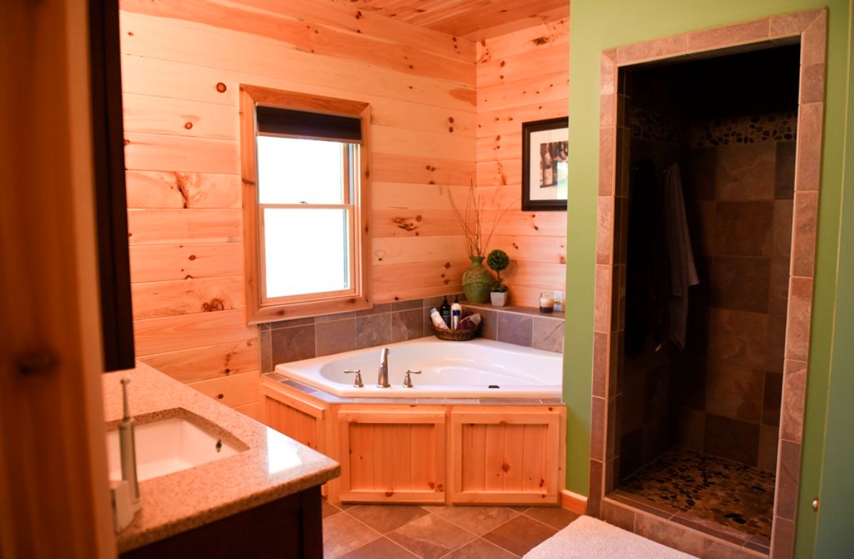 view looking into log cabin bathroom with white jacuzzi tub in corner and green walls in foreground