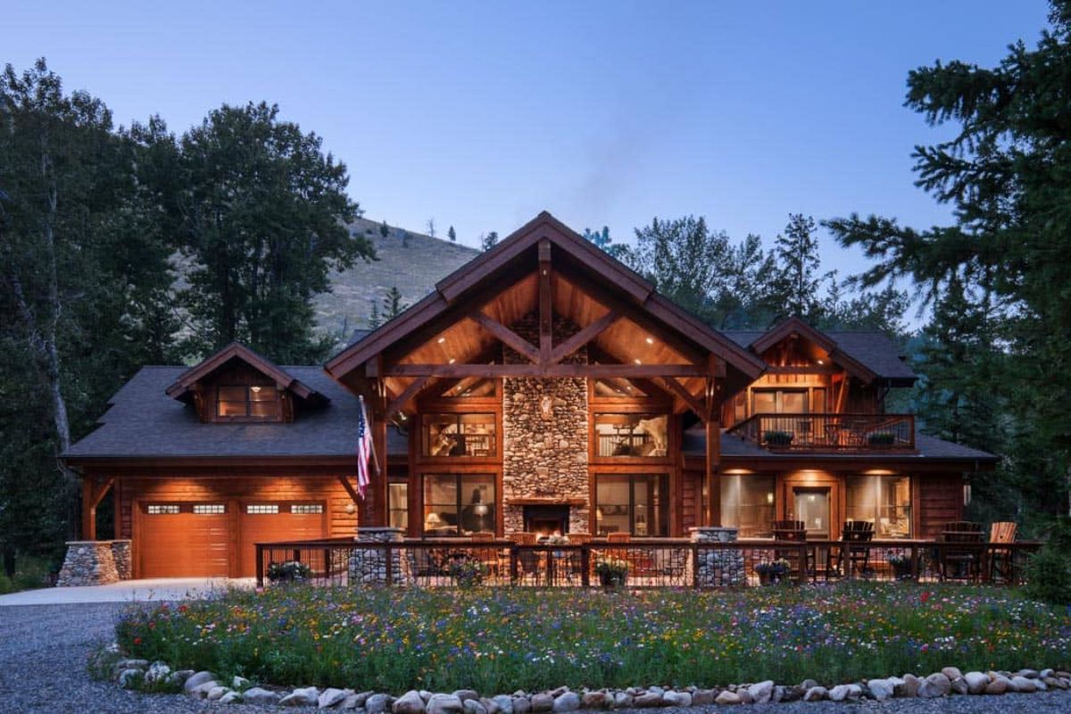 log cabin with two car garage on left and fireplace in center under awning