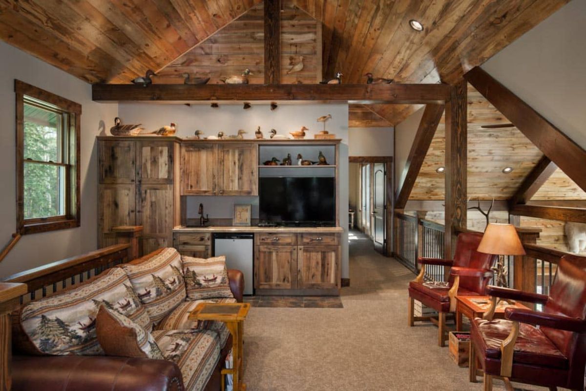 rustic wood sofa with cushionso n left and television on back wall with red chairs on right