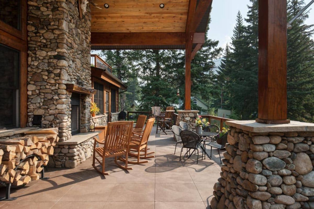 view across covered deck with stone fireplace on left and stone wall on right