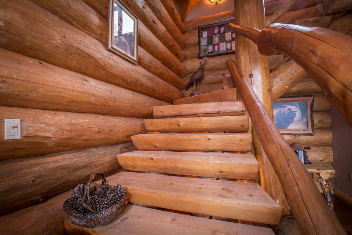log stairs to second floor of log cabin with shooes at base of stairs