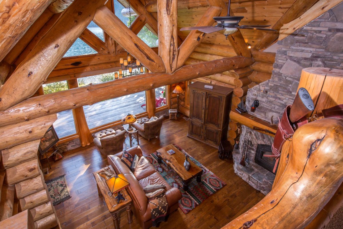 view from loft down into log cabin living area with stone fireplace on right and sofa in middle
