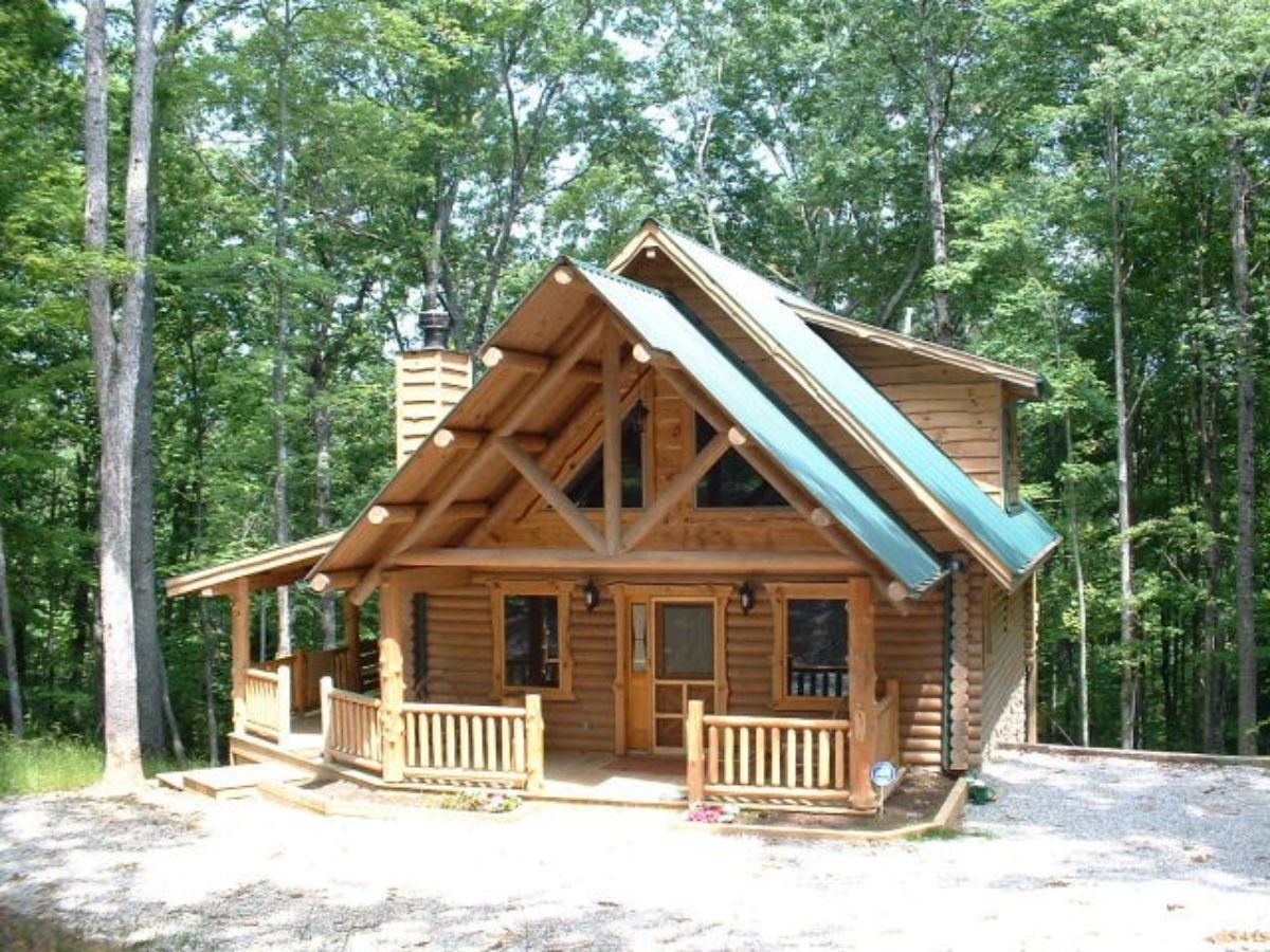 small cabin with light wood siding and railing and trees in background