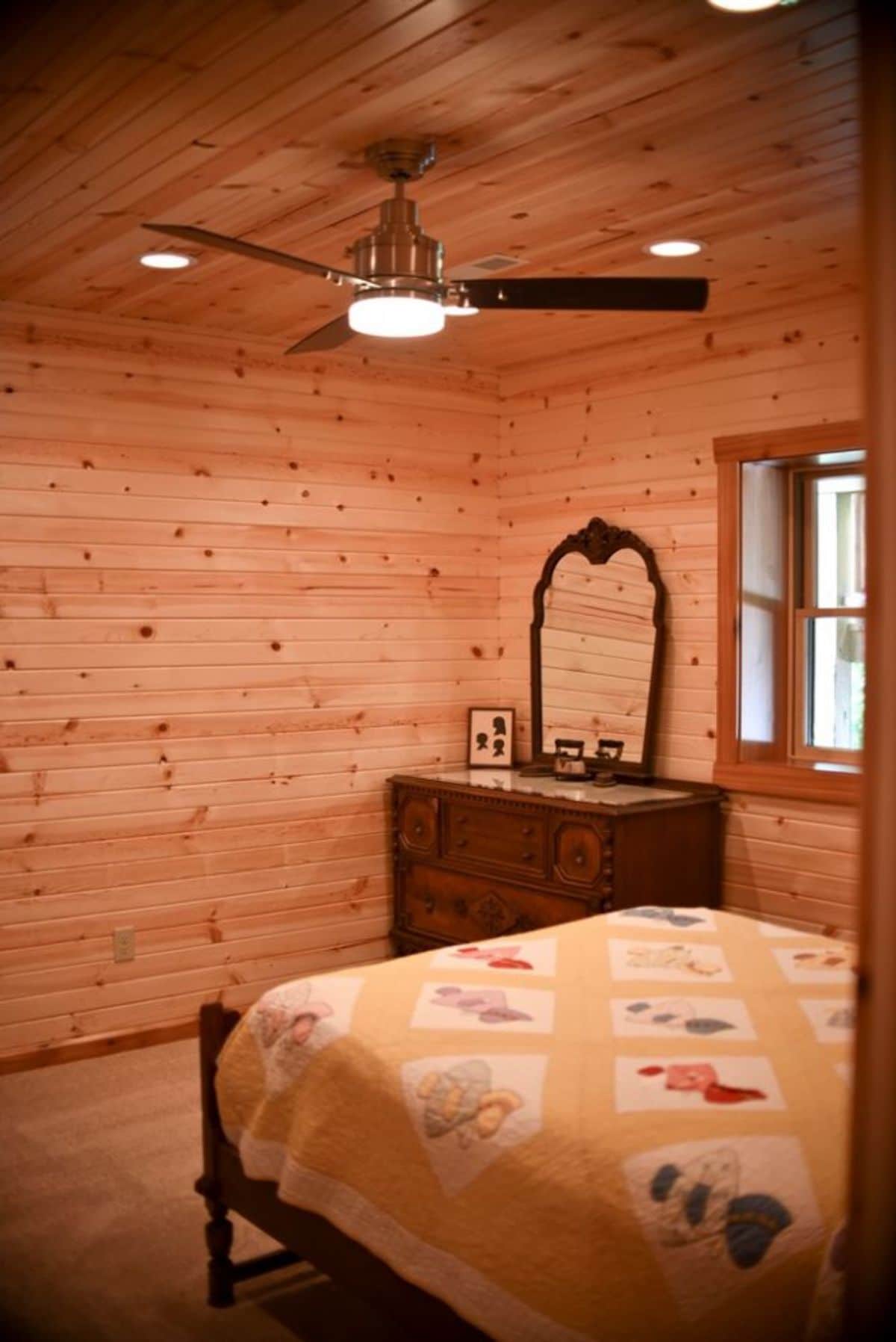 bed on right with dresser in back left corner of log cabin
