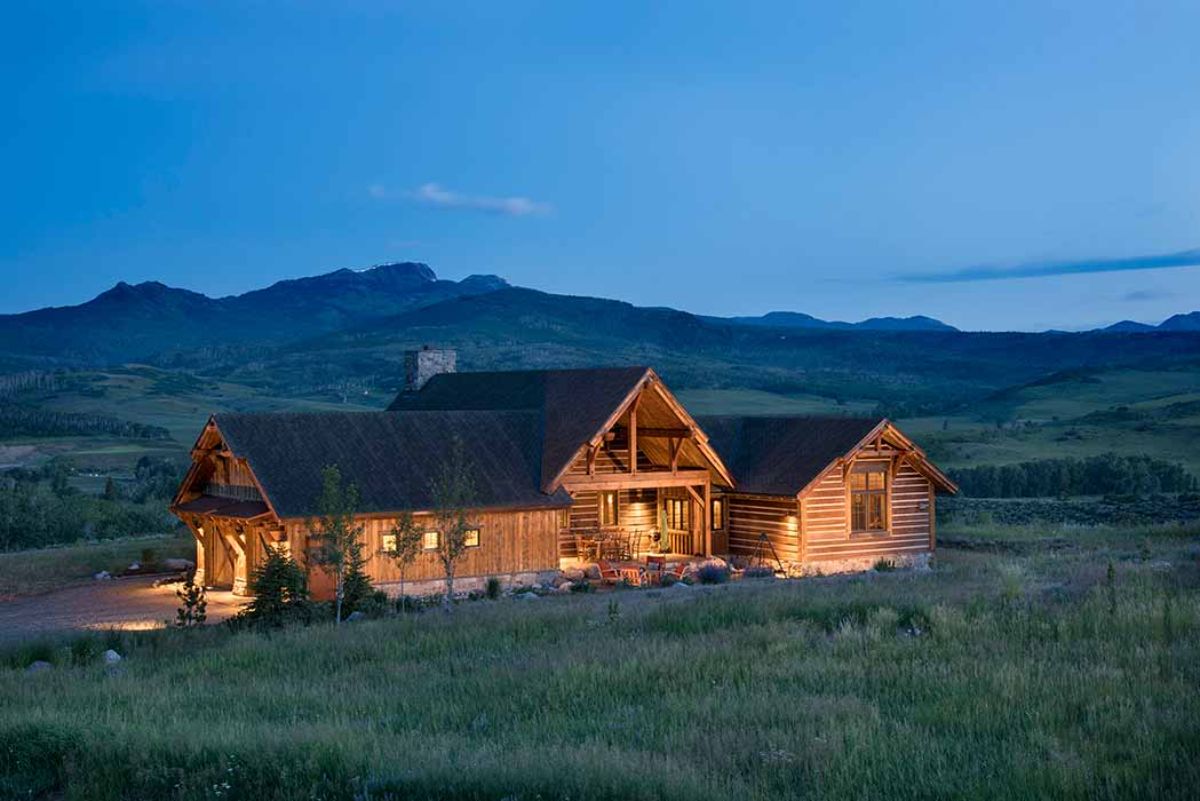 sprawling log cabin with hills in background lit up after dark