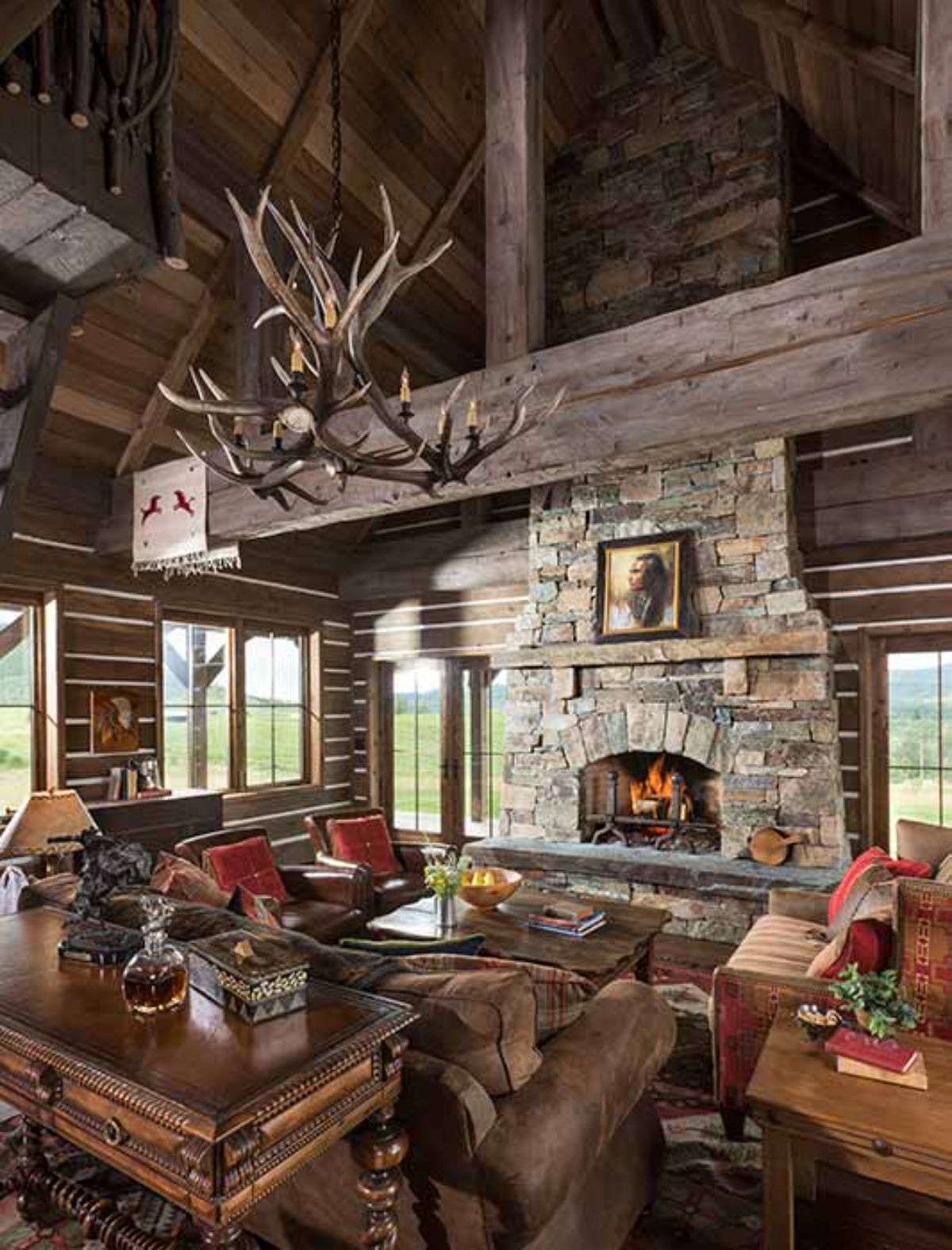 stone fireplace on right side of image with windows on both sides and brown leather chairs in foreground