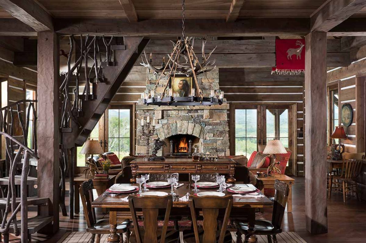 dark wood table and chairs with stone fireplace in background and antler chandelier above