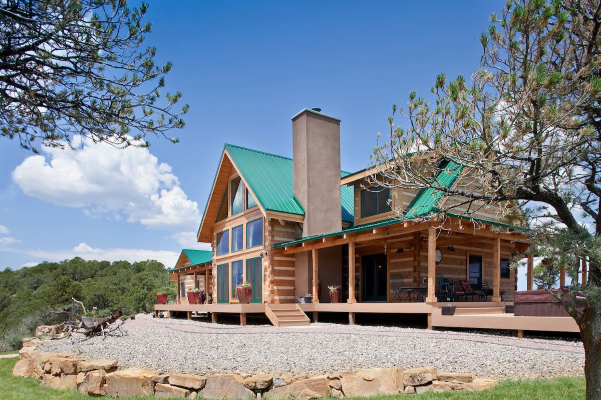 covered porch next to wall of windows on back of log cabin with chimney on top