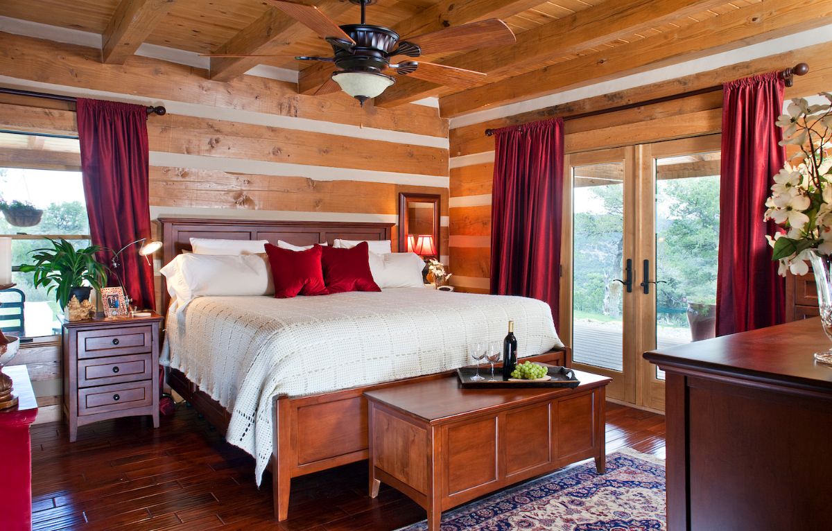 white linens with red pillows on bed with wood chest at end and patio doors on right