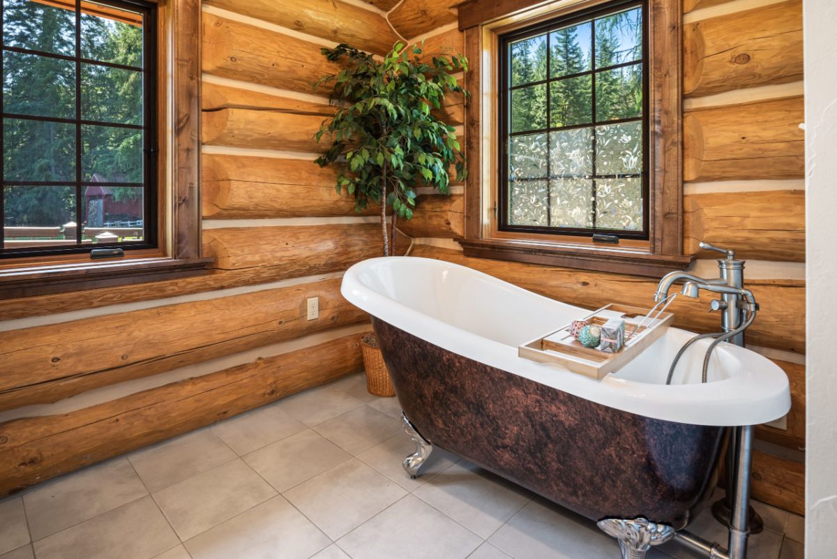 brown and white soaking tub in corner of log room with window above to the left