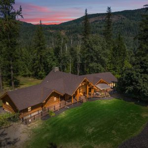 drone view of log cabin from above with mountains and sunset in background