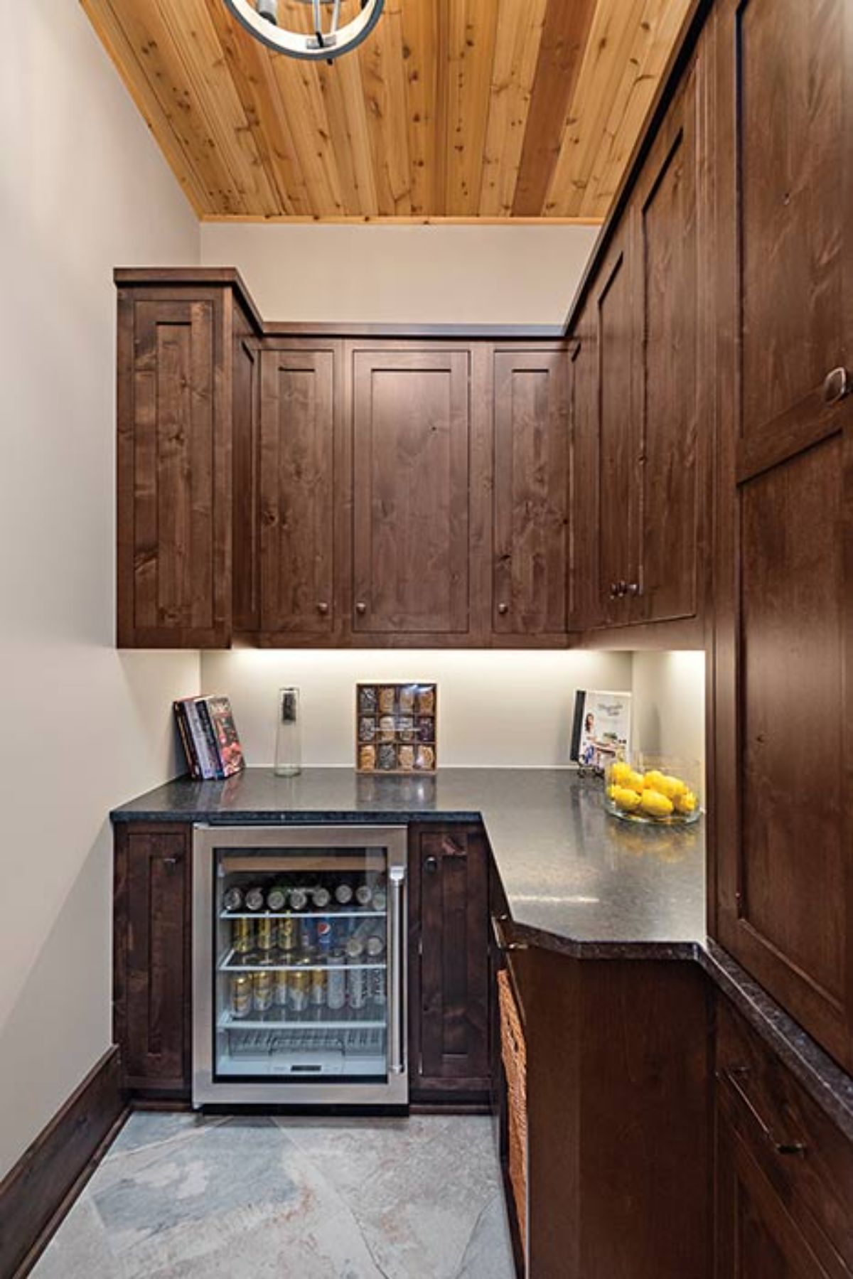 wine fridge at back wall of pantry with dark wood cabinets and white walls