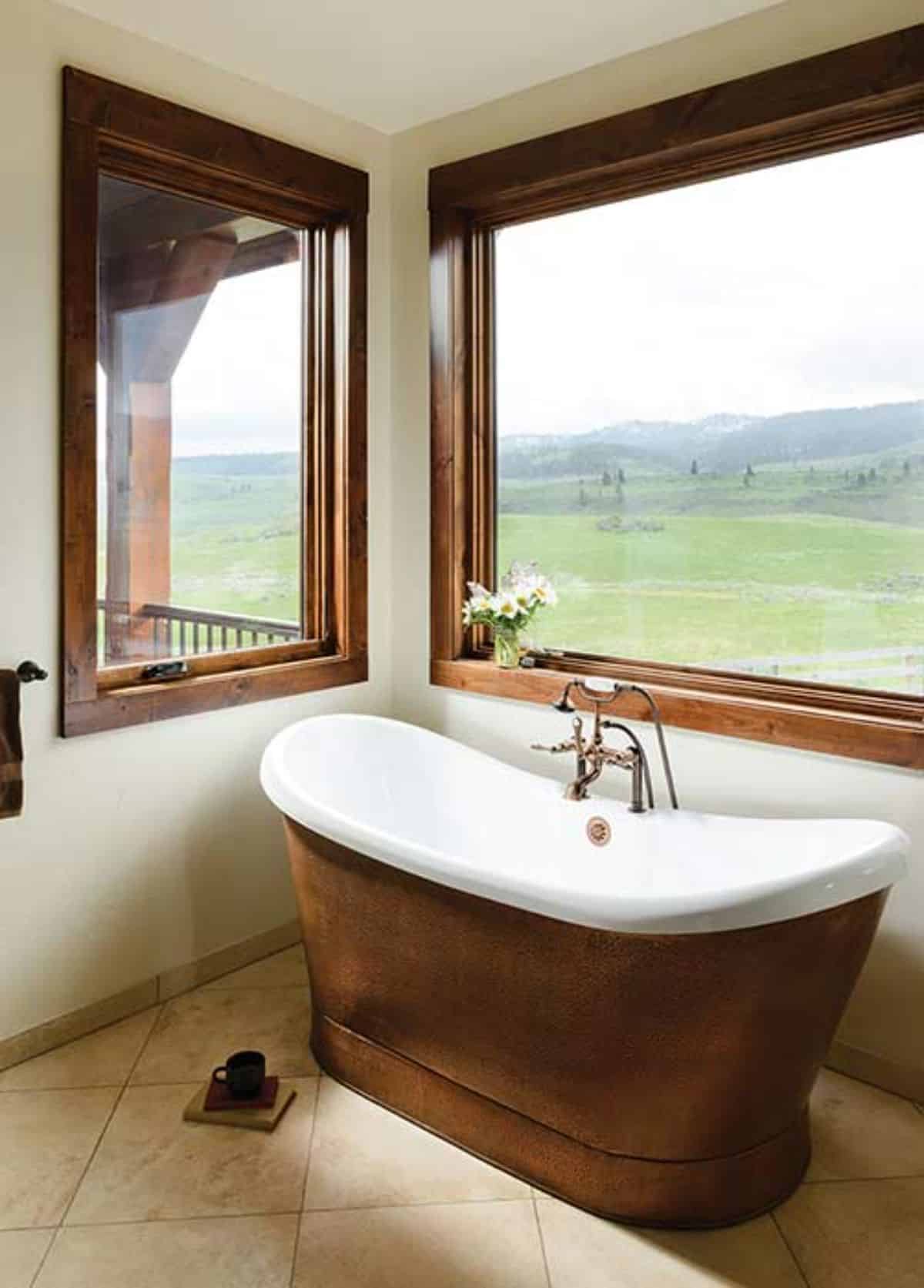 copper base on white soaking bathtub under picture window in bathroom with white walls