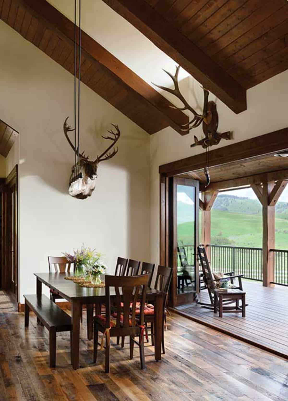 dining table underneath skylight with deer antlers and head agaisnt wall