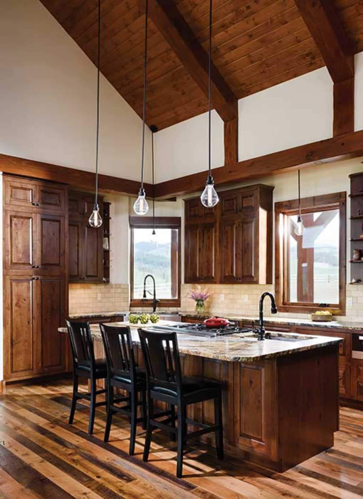 wood island with black high back stools and dangling lights above light marble counters