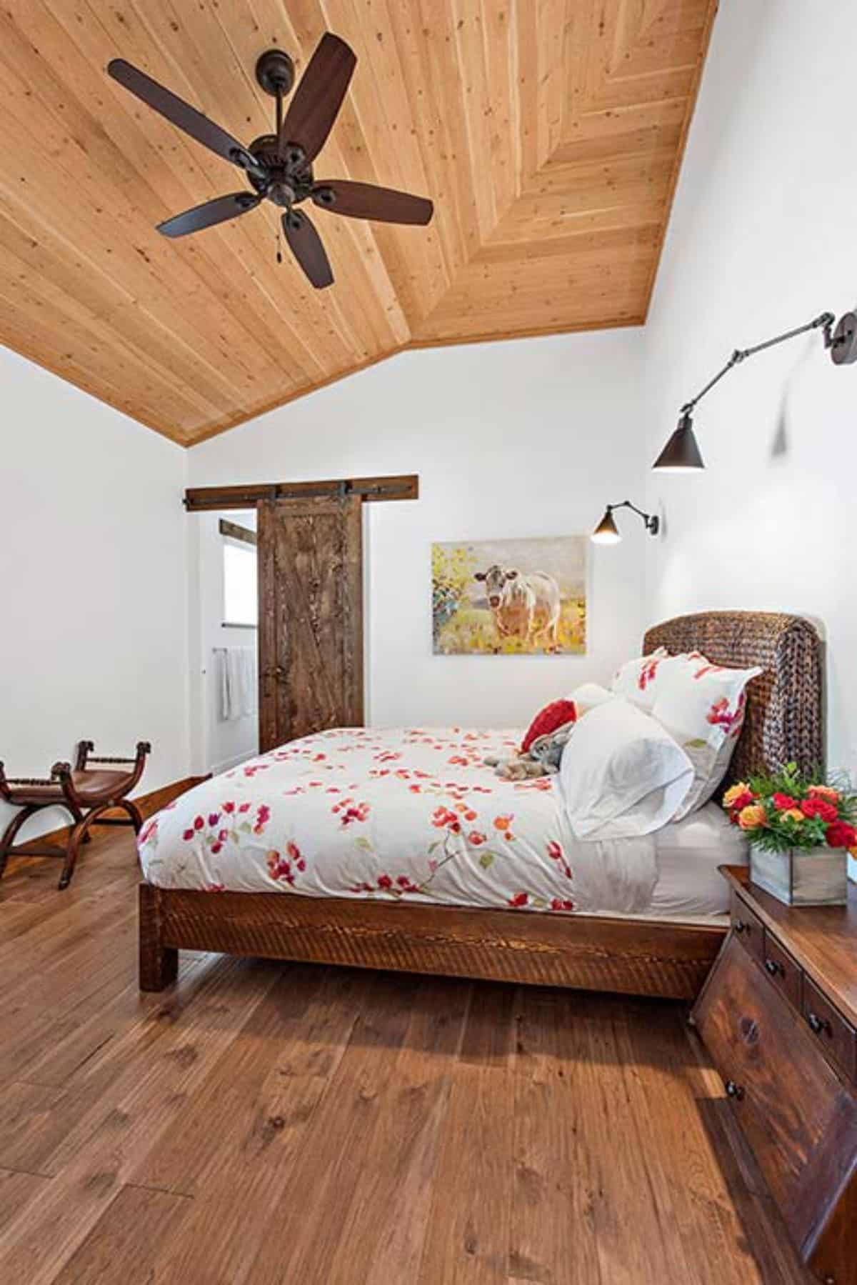 white and red floral bedding on bed with wood frame against white wall