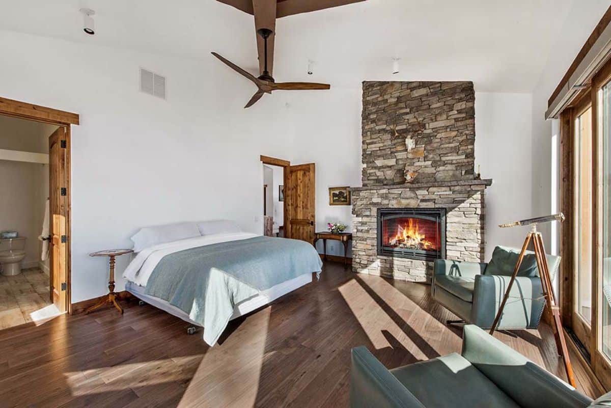 fireplace in corner of cabin bedroom with ceiling fan above bed