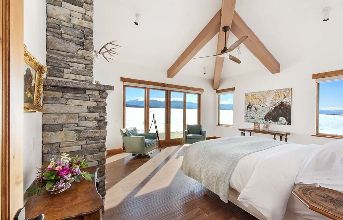 windows on wall next to fireplace with white linens on bed in foreground