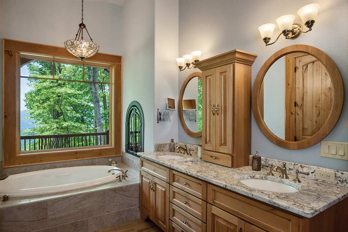 white soaking tub surrounded by tile in background with light wood cabinets in foreground