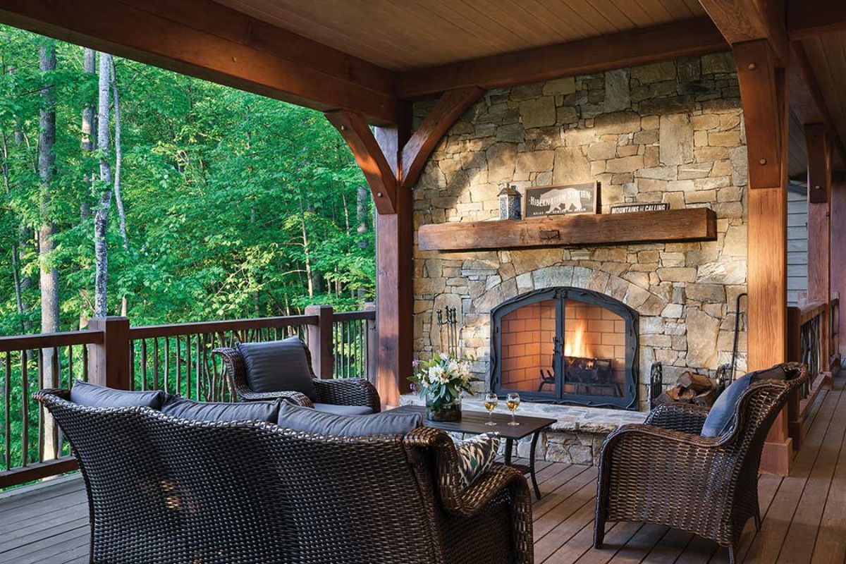 deck chairs in front of outdoor fireplace with roof above and wood railing on edge of porch