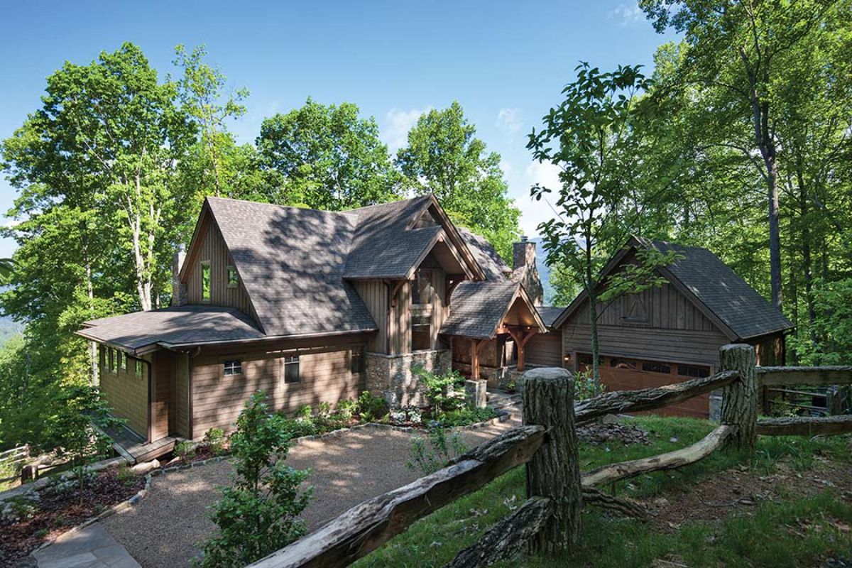 sprawling log cabin with paved drive and fence in foreground