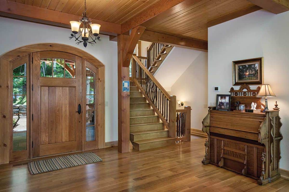 white walls and wood floors just inside cabin front door with chandelier above