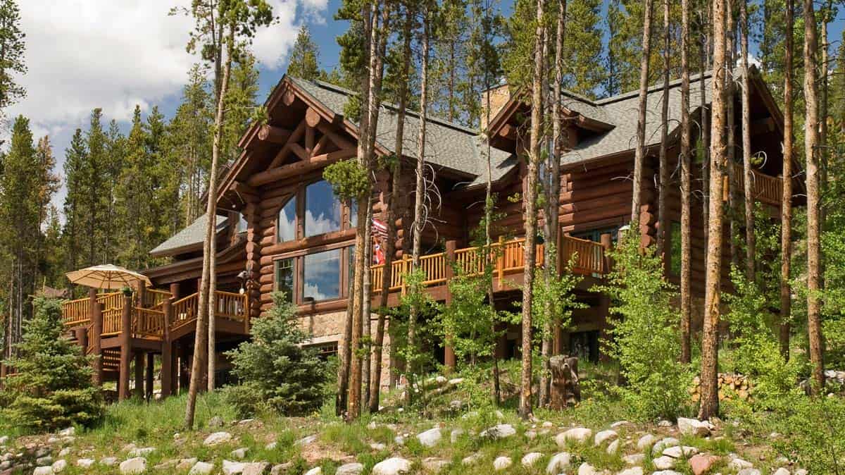 two story log cabin with decks behind tree line