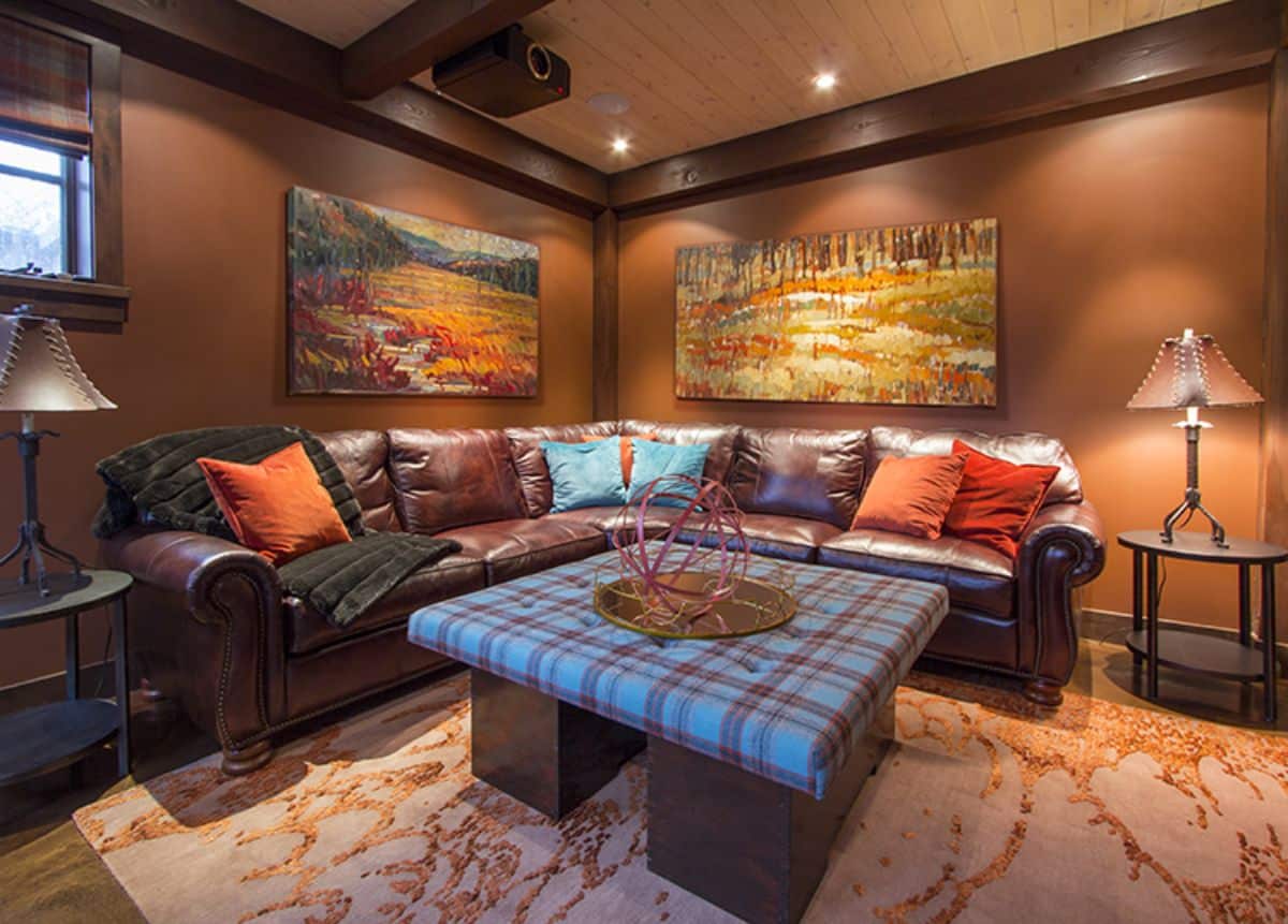 upholstery covered square table in front of brown leather sectional with bright throw pillows