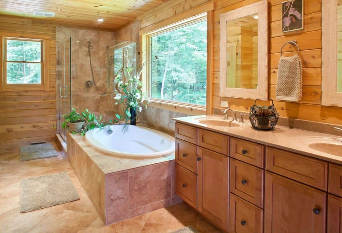 soaking bathtub under window with light brown tile surrounding and medium stain wood cabinets